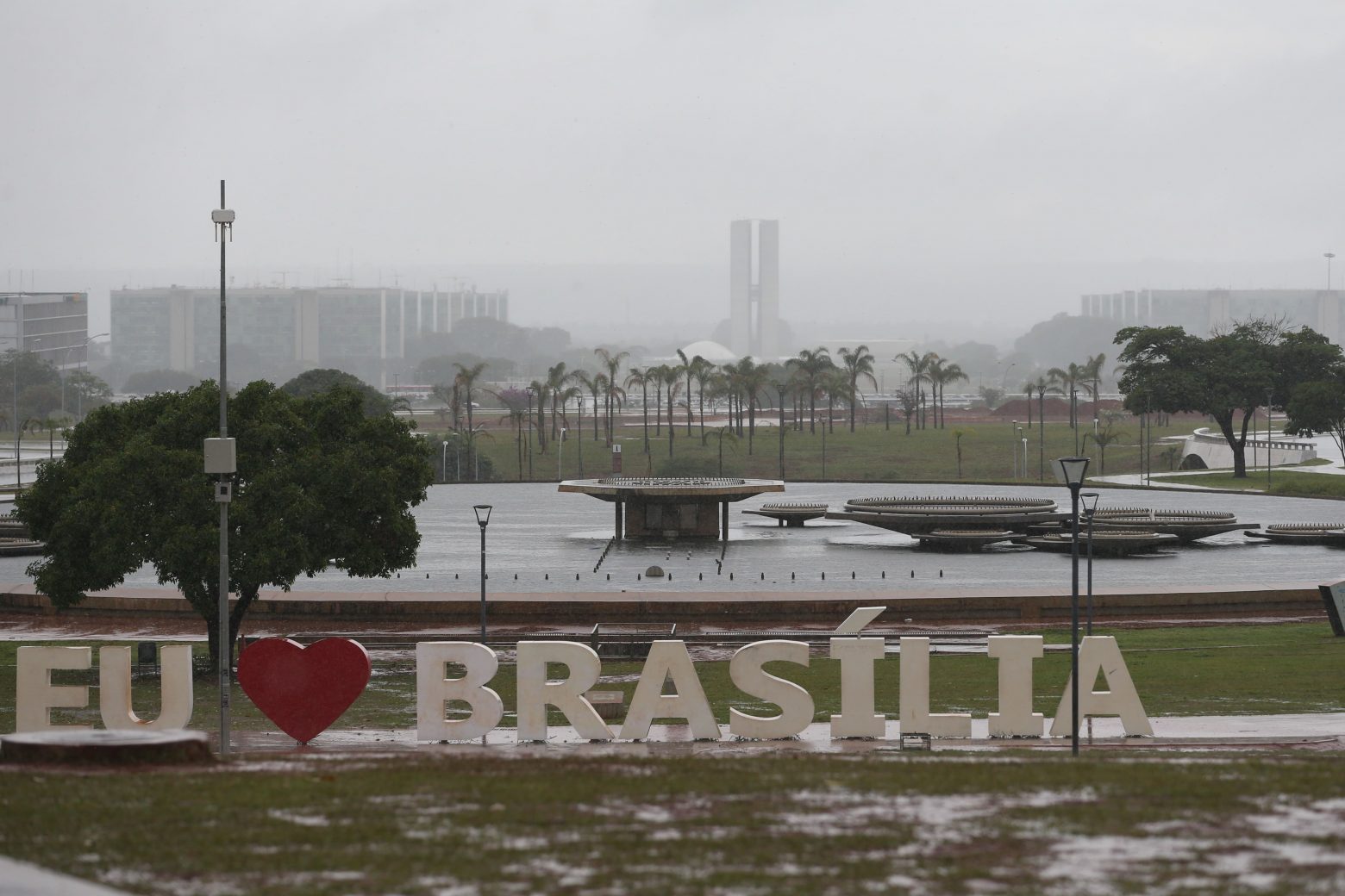 Placa Eu amo Brasília, Fonte desligada e Congresso Nacional ao fundo. Dia de chuva, céu nublado.