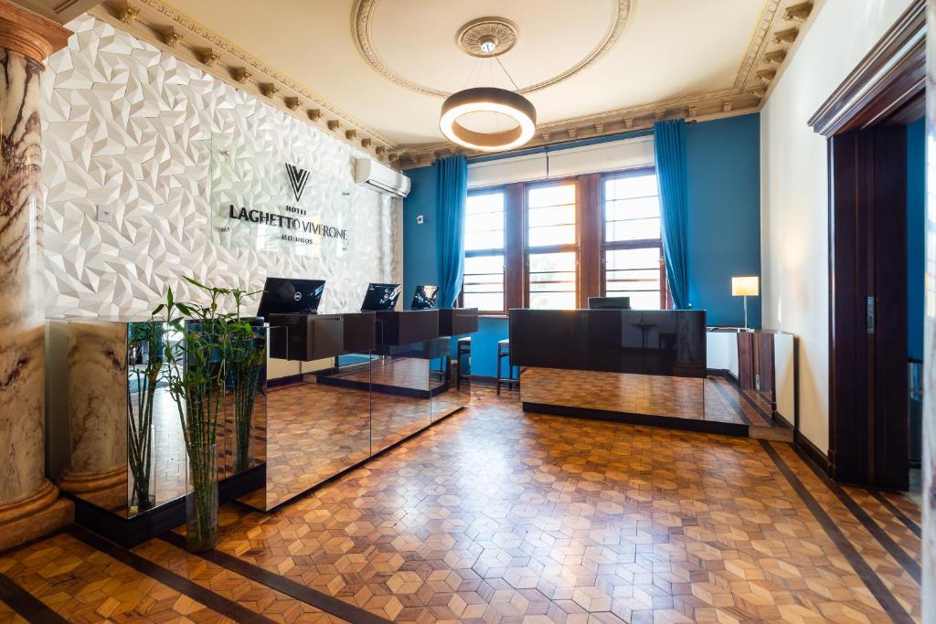 Recepção do Hotel Laghett e Porto Alegre. Na imagem aparece computadores, cortina azul com janela ao fundo e piso de taco na cor marrom.