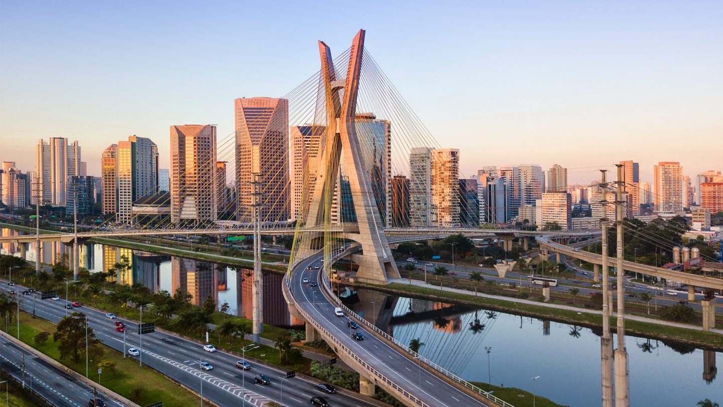 Ponte e prédios altos no fundo. Carros na pista e rio. São Paulo.