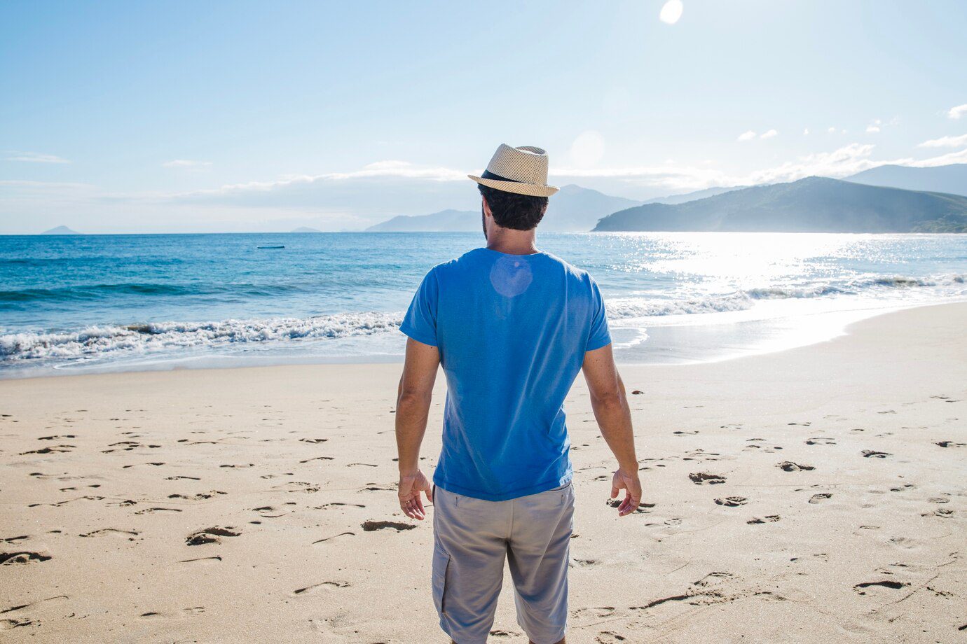 Homem de chapéu na praia, olhando o mar. Banco de Imagens.