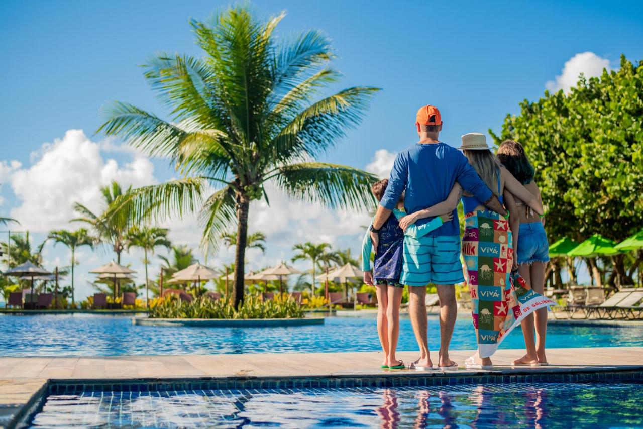 Dois adultos e duas crianças abraçados de frente para piscina - Vivá Porto de Galinhas Resort 