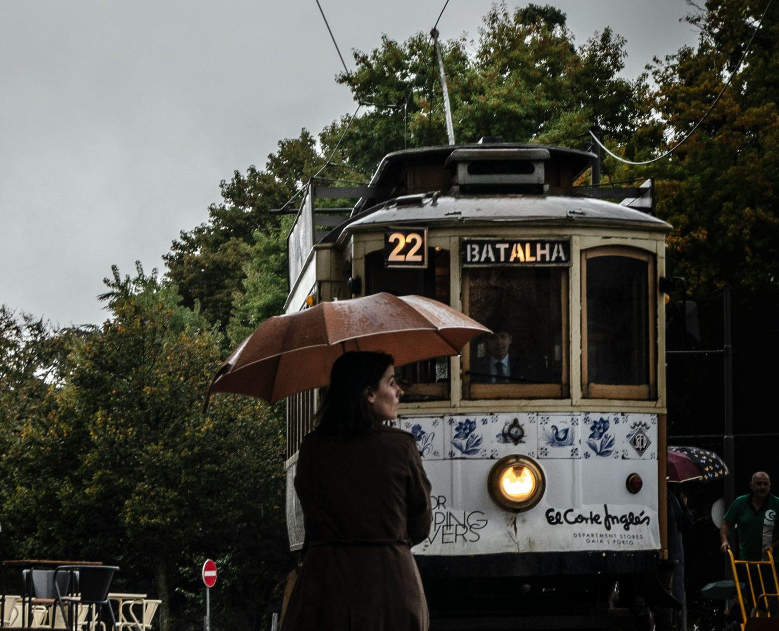 Mulher com guarda-chuva na frente de um bondinho elétrico que vai para Batalha. Porto, Portugal.