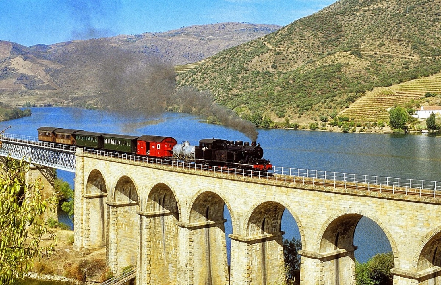 Comboio Histórico do Douro passando por uma ponte e rio ao fundo.