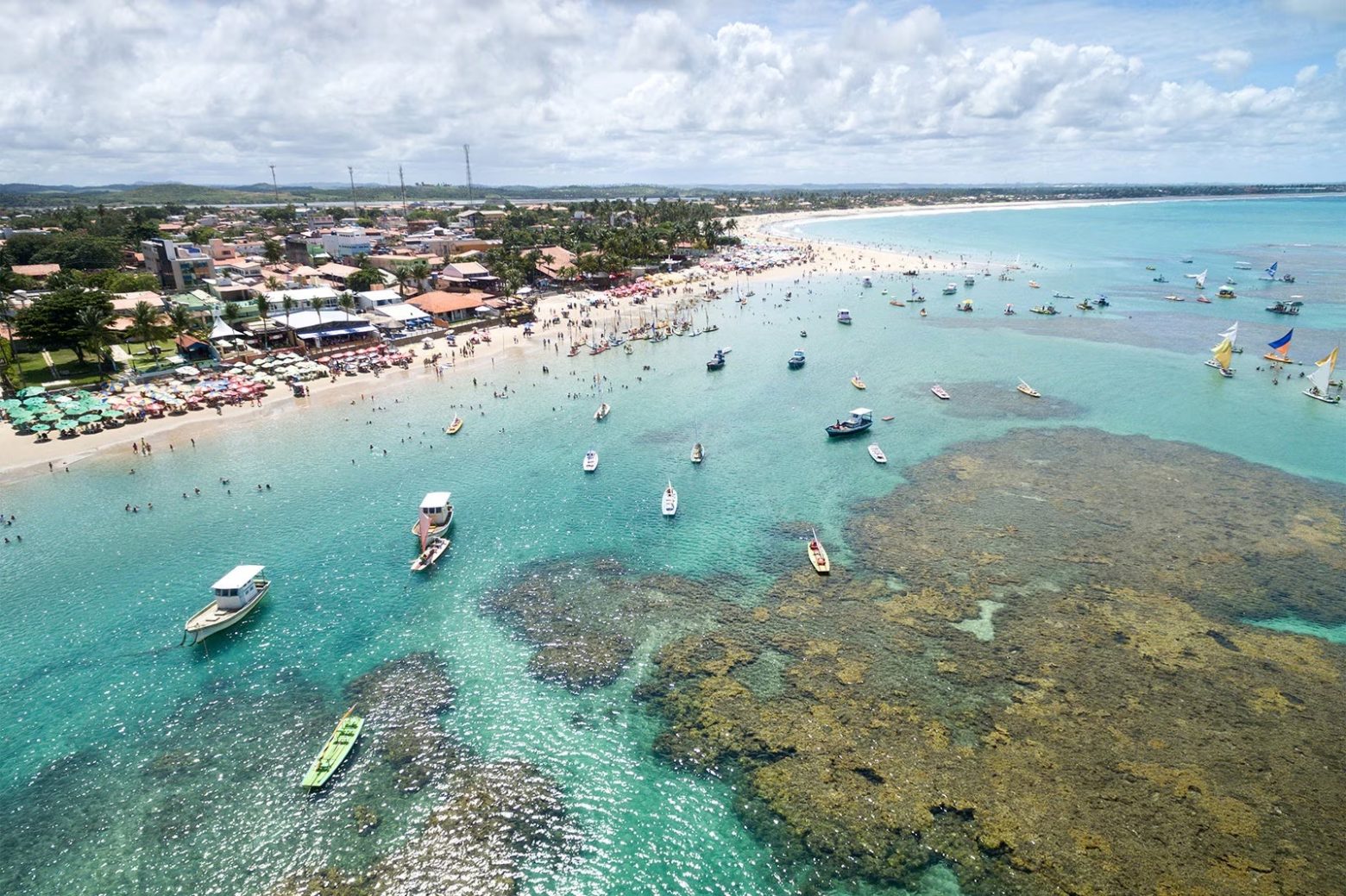 Imagem da Praia do Nordeste no Brasil - Barcos sobre o mar, e casas atrás das areias da praia.