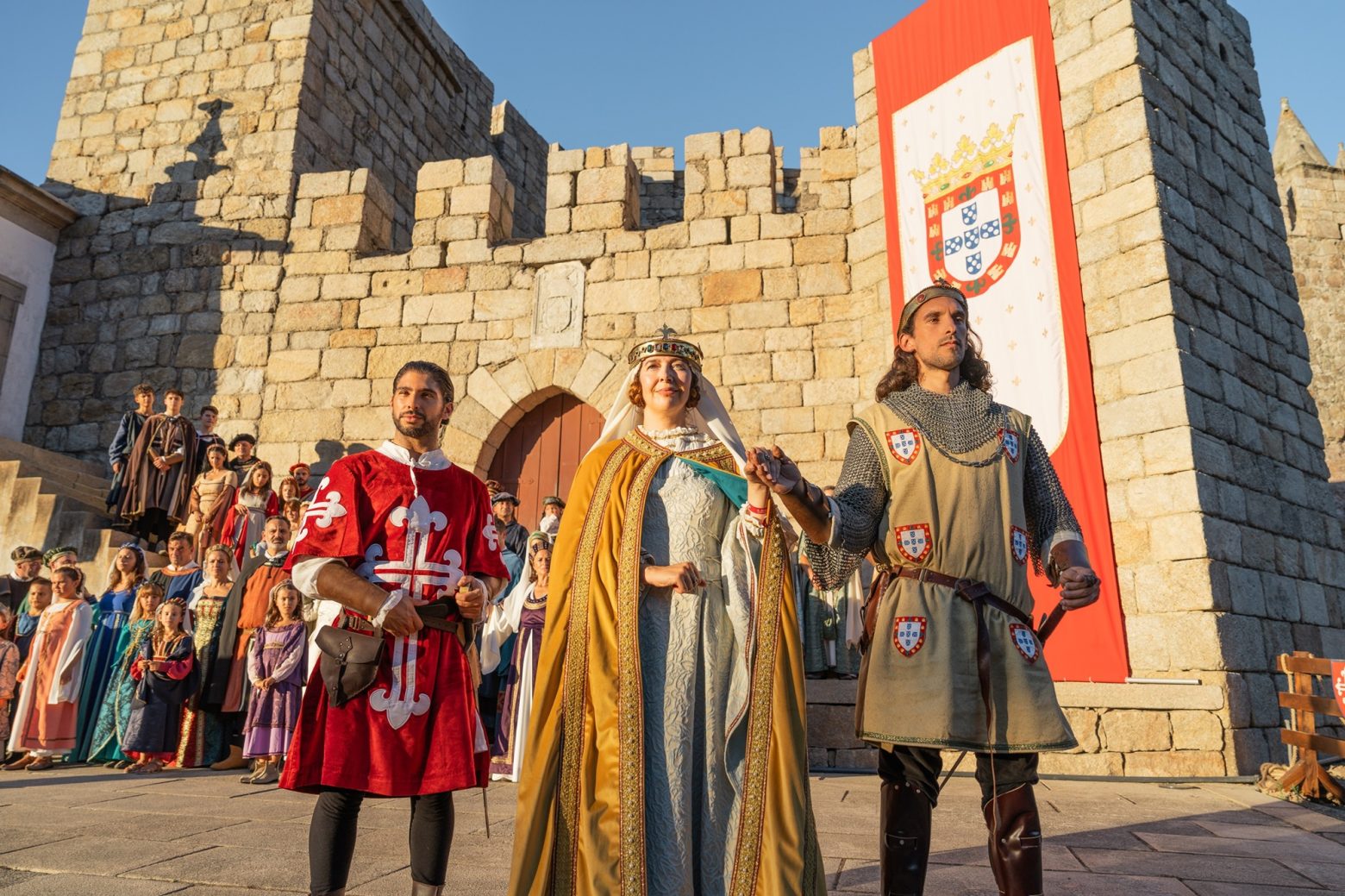 Pessoas caracterizadas com roupas medievais, castelo ao fundo. Viagem Medieval em Terra de Santa Maria