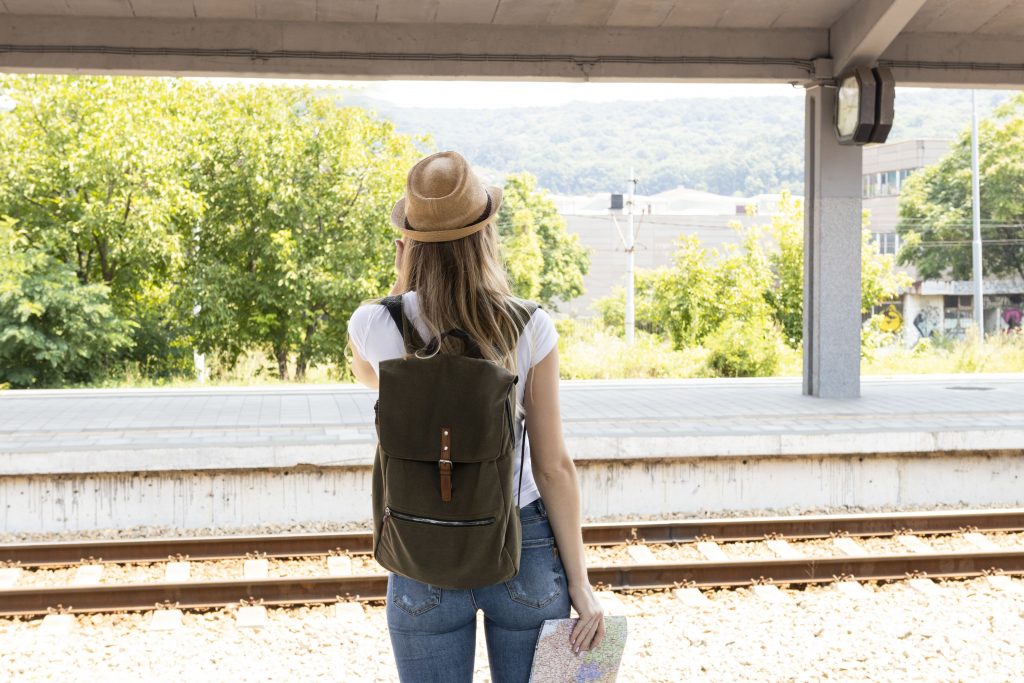 Banco de imagens. Mulher com mochila numa estação de trem. mapa na mão e chapéu.