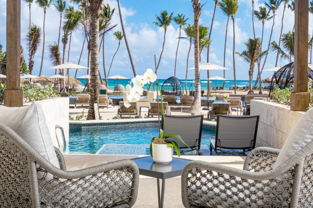 Mesa, cadeiras, espreguiçadeiras, piscina, mar ao fundo e coqueiros. Resort Punta Cana All Inclusive.
