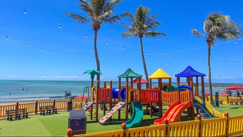 Parquinho Vô Hélio - Maceió - coqueiros, brinquedos coloridos, mar ao fundo