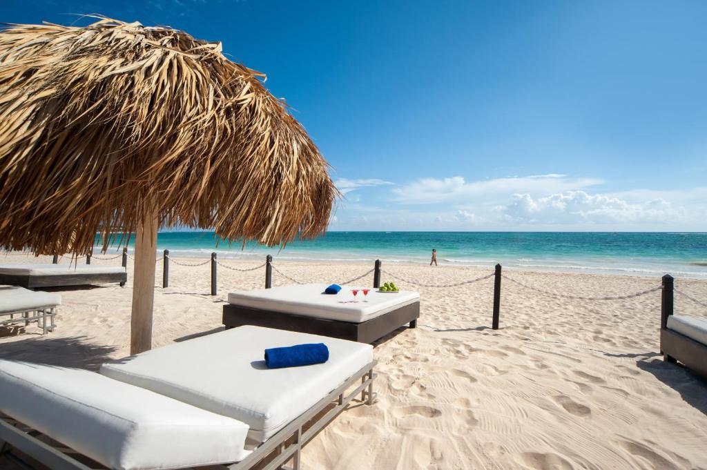 Espreguiçadeira branca, com toalha azul enrolada, guarda-sol de palha. Areia branca e mar da cor esmeralda. Punta Cana.