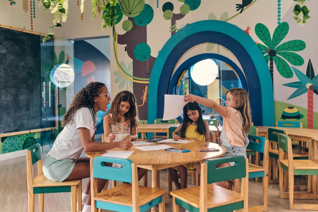 Recreação do Iberostar Selection Praia do Forte - monitora sentada na mesa com três crianças, brinquedoteca