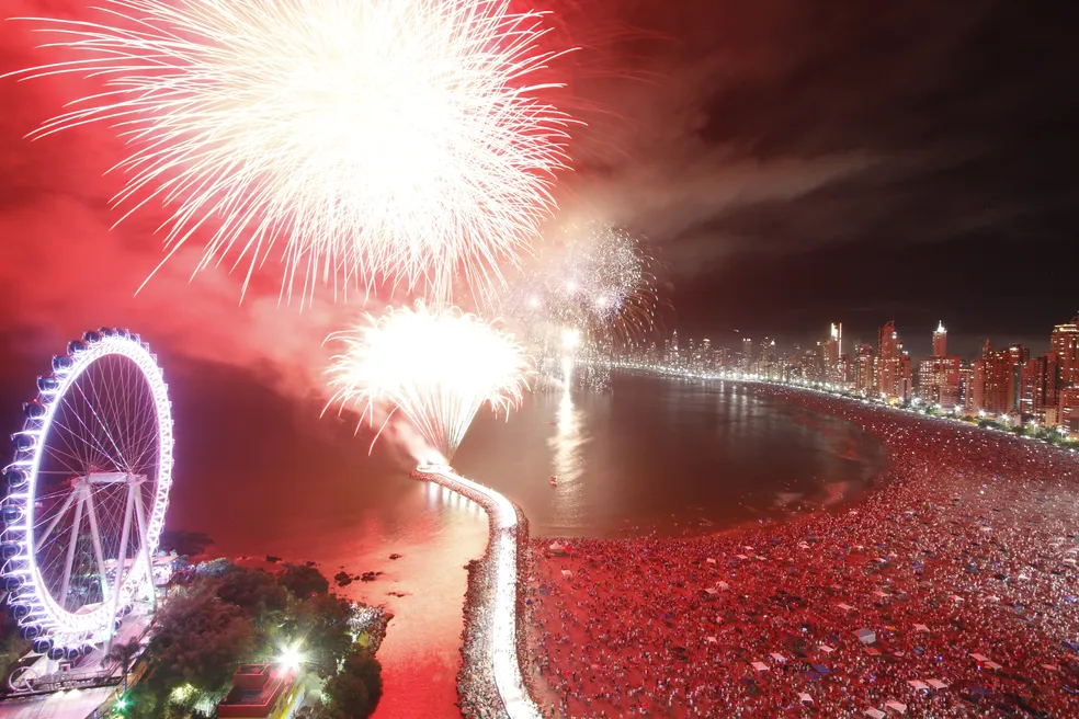 Fogos de artificio em Balneário Camboriú - A imagem mostra o Reveillon na cidade com pessoas na areia da praia.