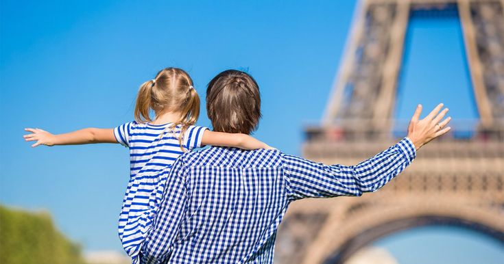 Uma imagem de um pai com a filha no colo mostrando a Torre Eiffel. 