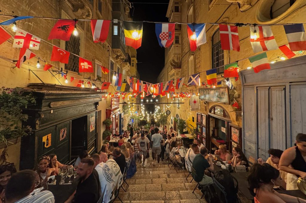 Uma foto mostrando uma rua cheia de pessoas comendo em mesinhas de restaurantes. 